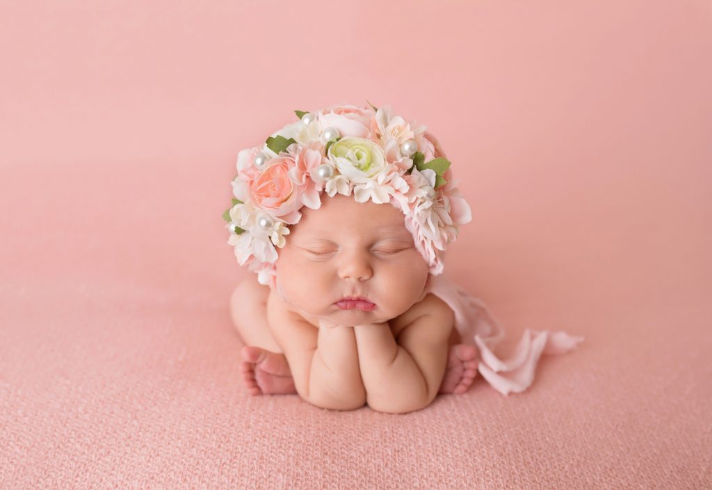 Newborn girl froggy pose with large floral bonnet.