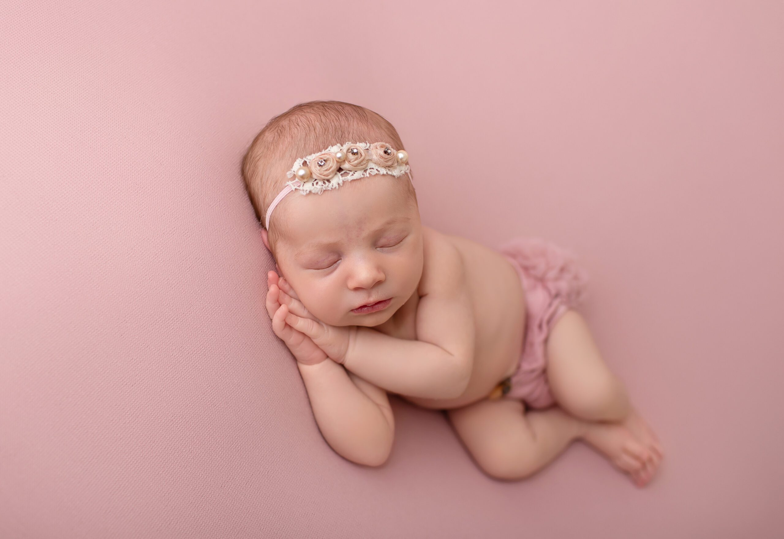 Newborn baby girl Brooklyn posed on a soft pink backdrop wearing a pearl and lace headband during her College Station, TX newborn session.