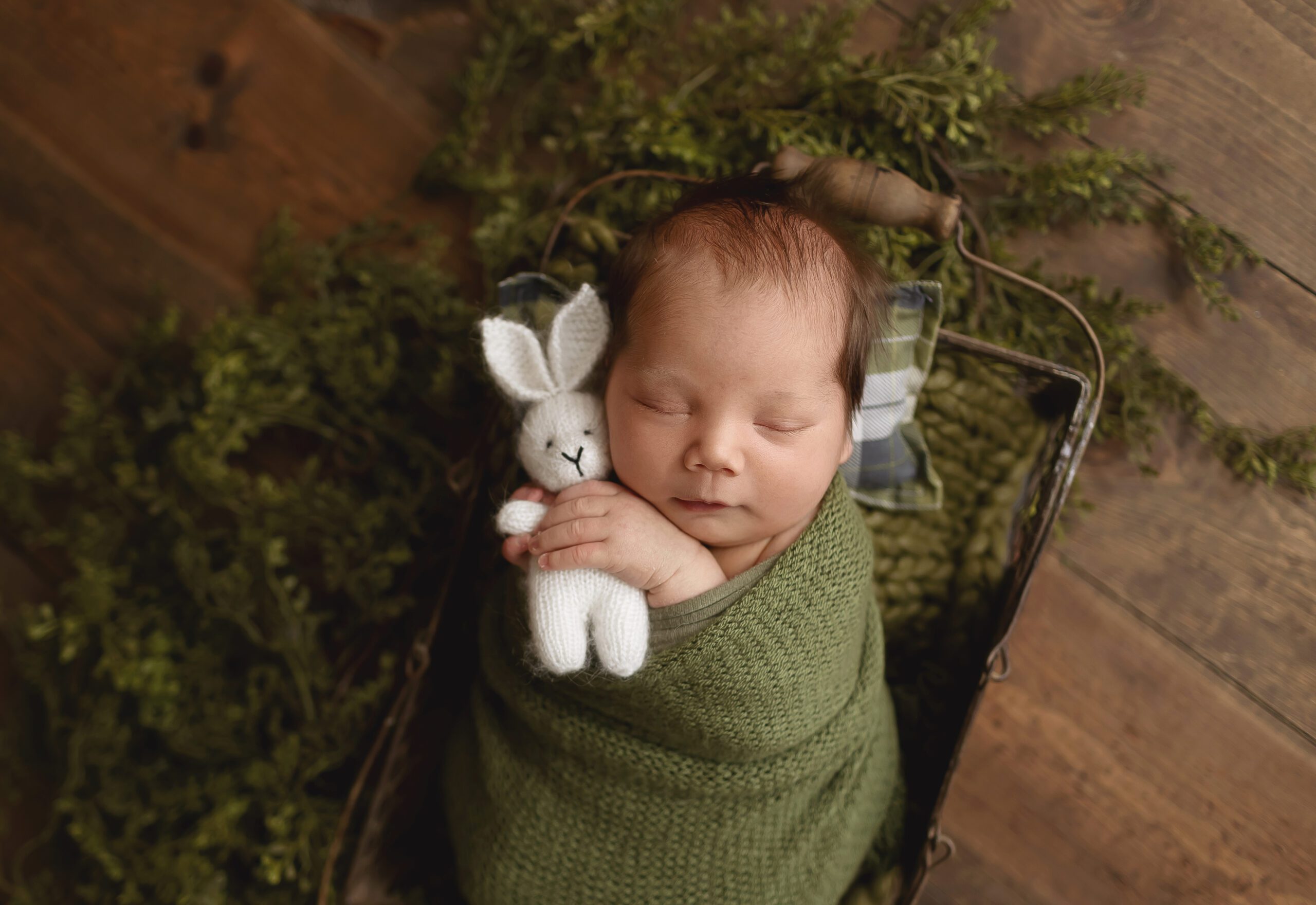 Newborn baby boy wrapped in green swaddle holding a white bunny stuffy during studio session in College Station, Texas
