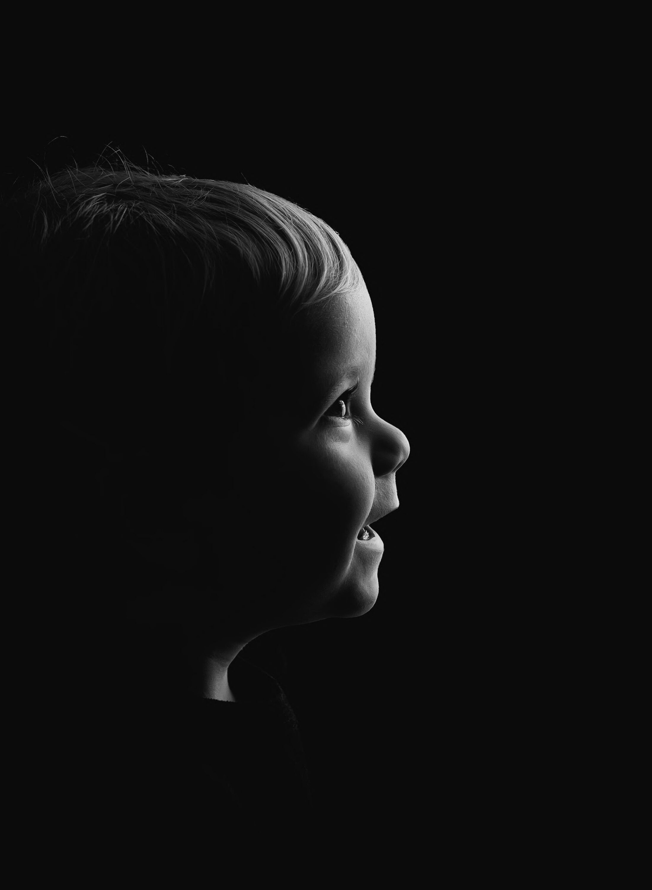 Young child smiling softly in side profile against a dark background.
