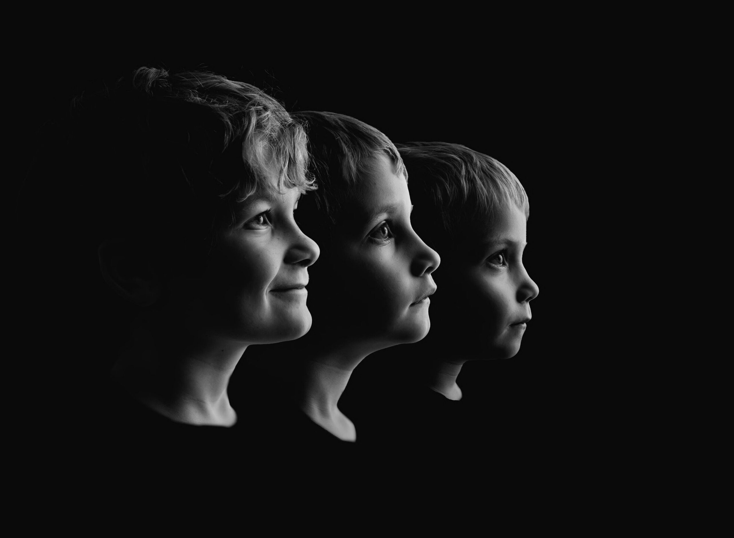 Three young boys photographed in side profile against a black background with dramatic studio lighting.