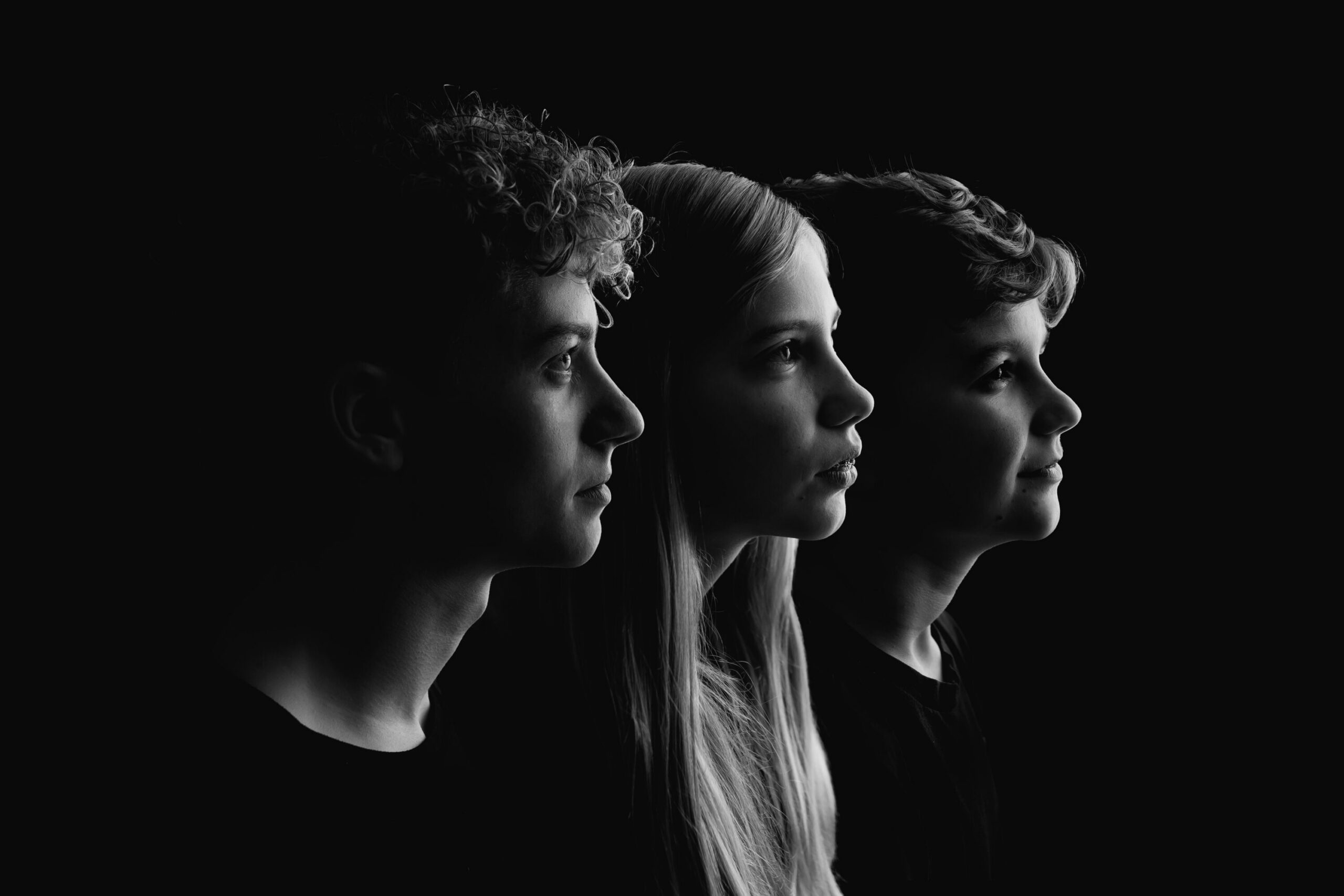 Three children arranged in side profile against a dark background with dramatic lighting.